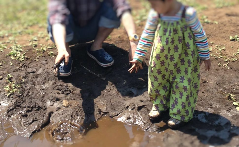 幼児がプレーパークでエプロンをかけて泥遊びをしているところ