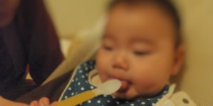 赤ちゃんが初めての離乳食をスプーンで食べているところ